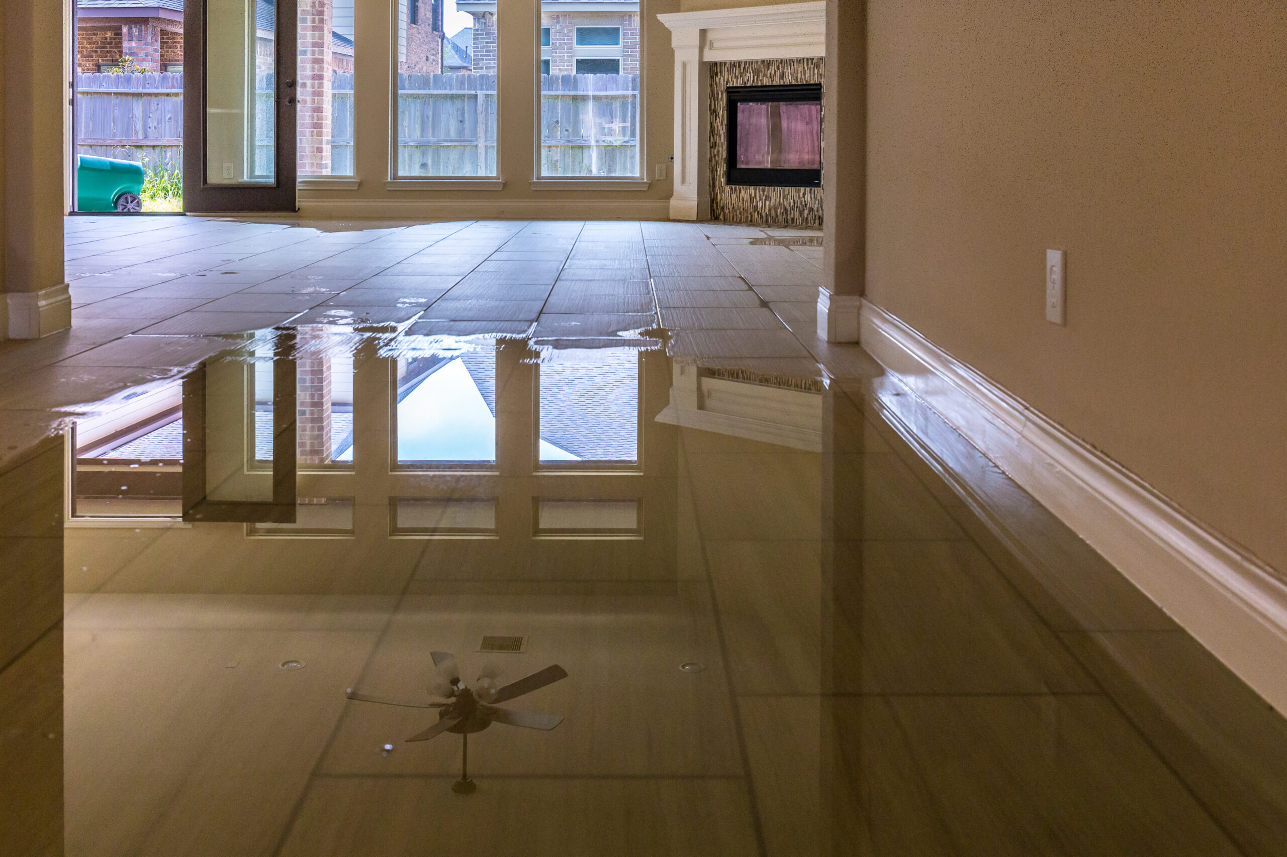 Flooded living room with standing water reflecting the ceiling fan and window
